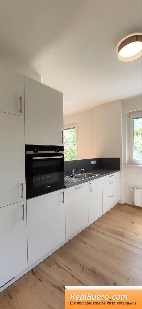 Helle Einbauküche mit weißen Schränken, integriertem Backofen und Holzboden.