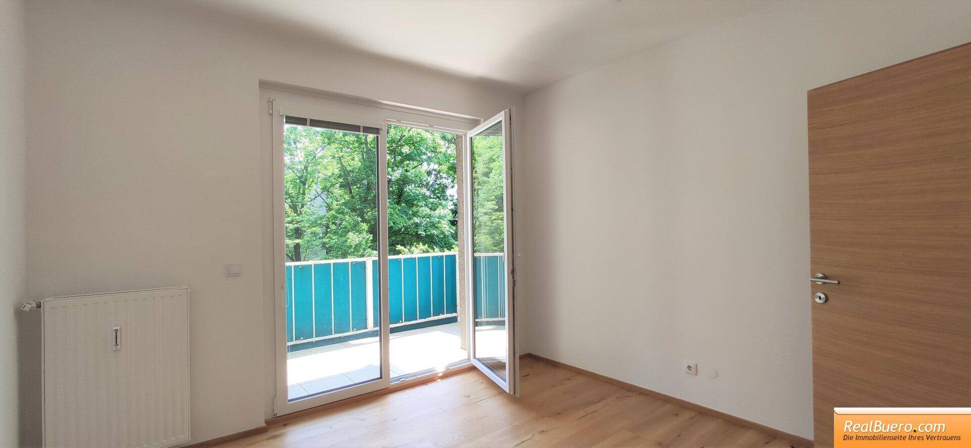 Helles Zimmer mit Balkonzugang, Holzboden und Blick ins Grüne.