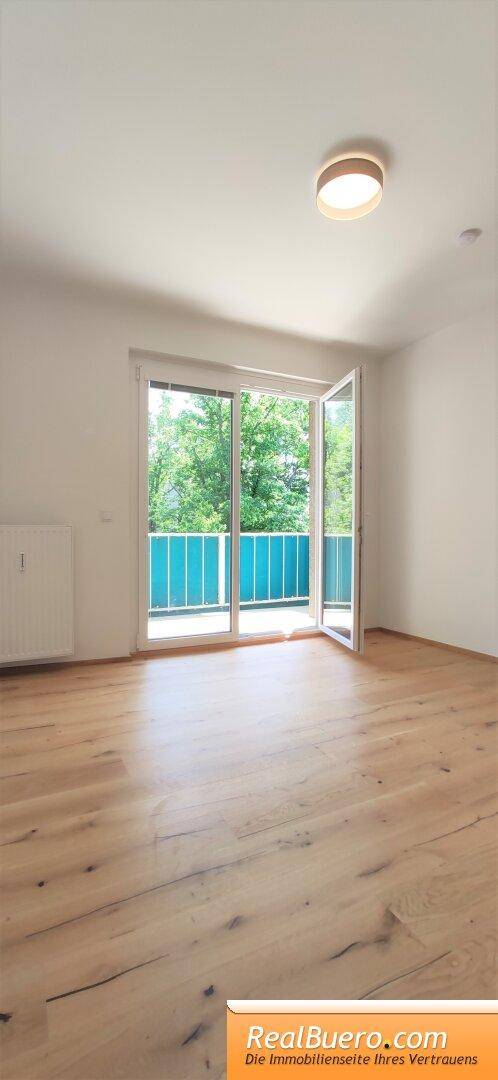 Geräumiges Zimmer mit Holzboden und Zugang zu einem sonnigen Balkon.