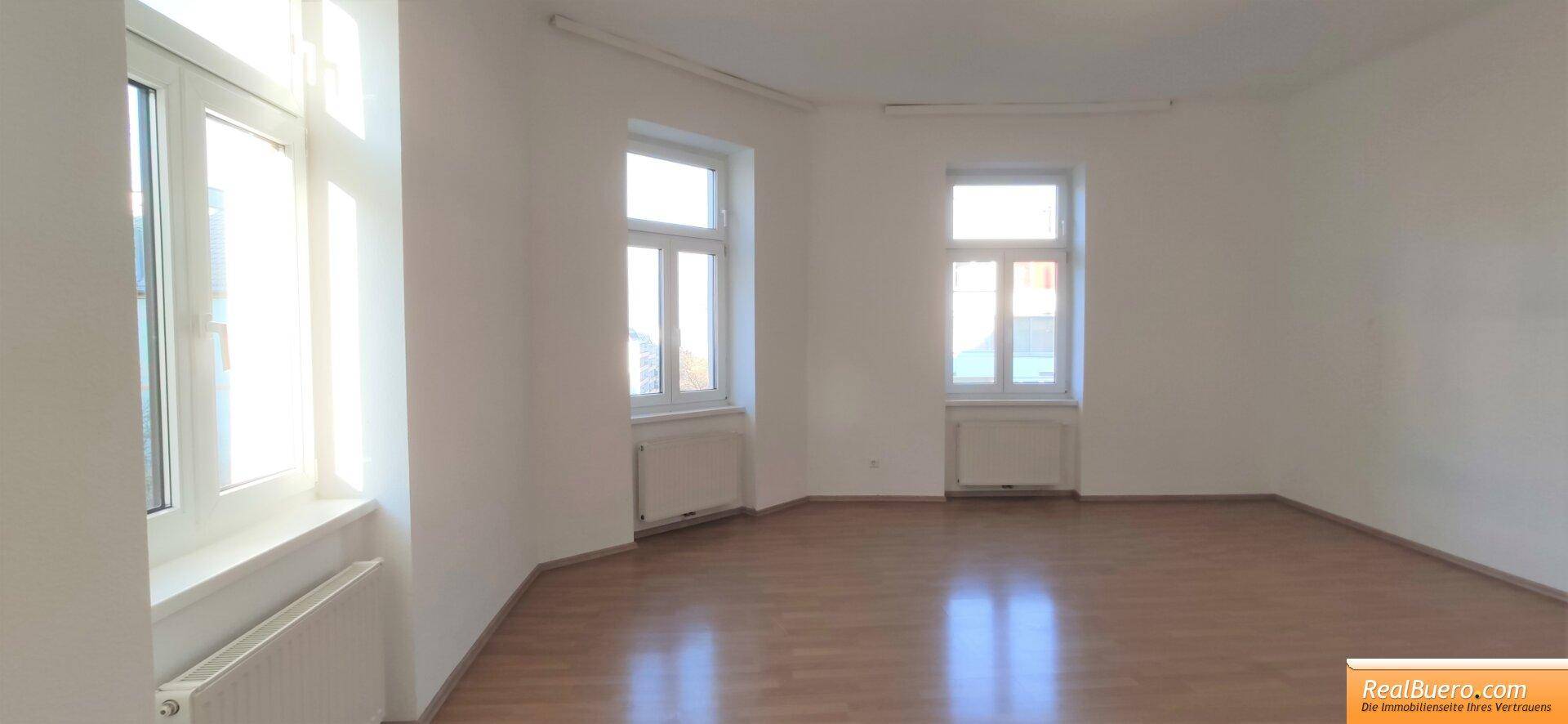 Geräumiges, helles Zimmer mit drei großen Fenstern und glänzendem Holzboden.