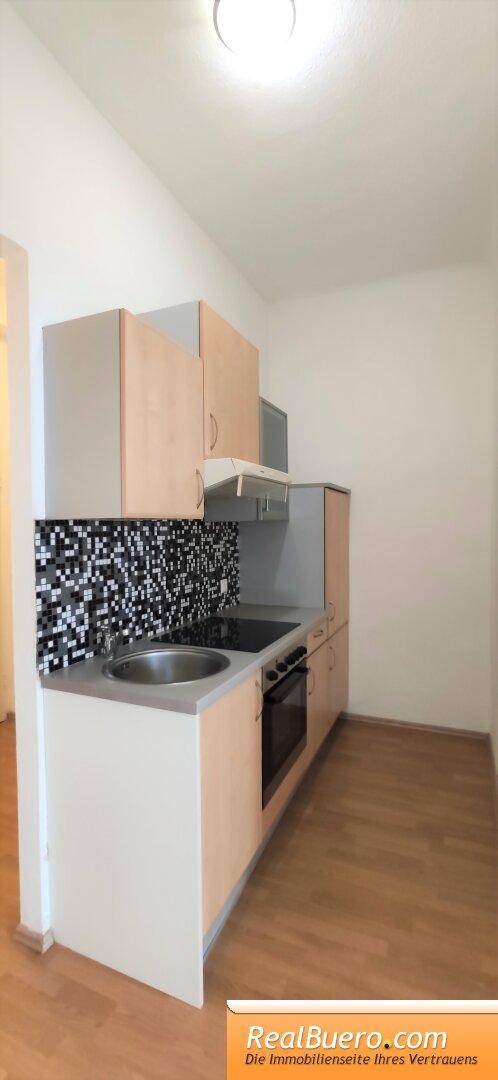 Kompakte Einbauküche mit hellen Holzschränken, Herd und Spüle, ideal für kleine Wohnungen.
