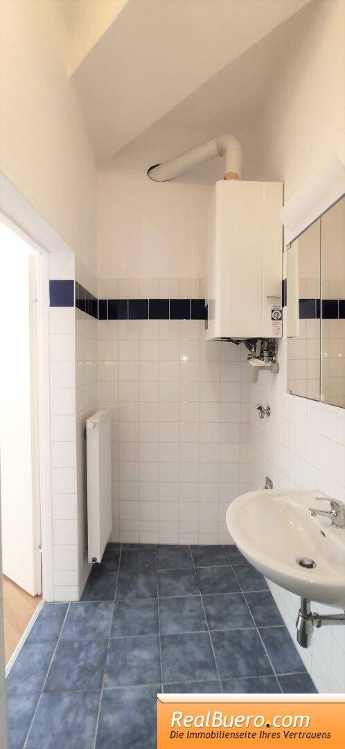 Badezimmer mit weiß-blauen Fliesen, Waschbecken und einem Wandspiegel.
