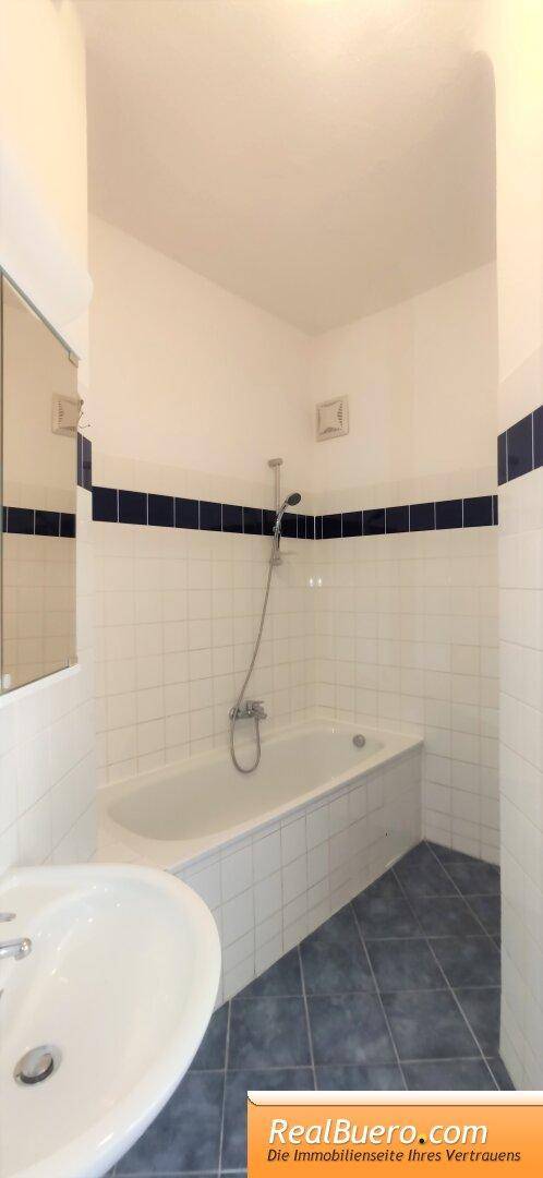 Badezimmer mit Badewanne, Duschvorrichtung und weiß-blauen Wandfliesen.