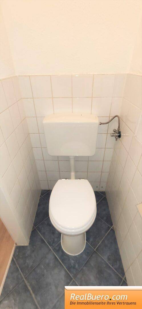 Separates WC mit Toilette, weißen Wandfliesen und blauem Fliesenboden.