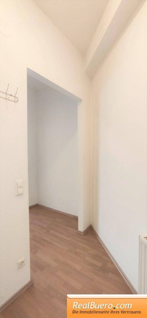 Heller Flur mit Holzboden und Garderobenhaken, der zu weiteren Räumen führt.