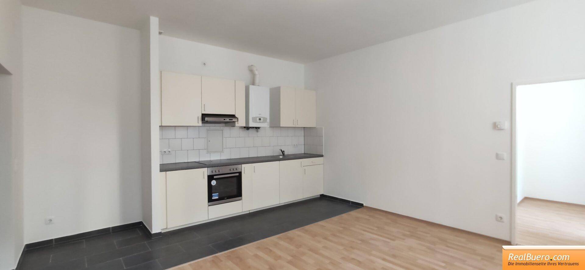 Offene Küchenzeile mit hellen Schränken und integriertem Backofen in einem geräumigen Zimmer.