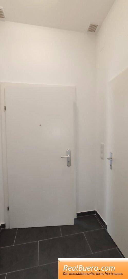 Eingangsbereich mit dunklen Fliesen und einer weißen Tür, die in die Wohnung führt und einladend wirkt.