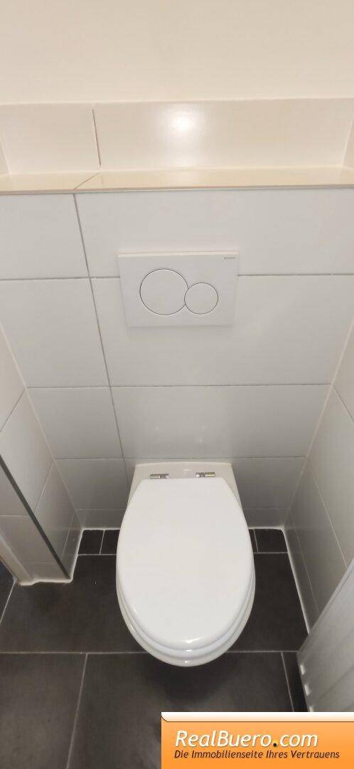 Separate Toilette mit Wand-WC und dunklen Bodenfliesen in einem funktionalen und sauberen Raum.