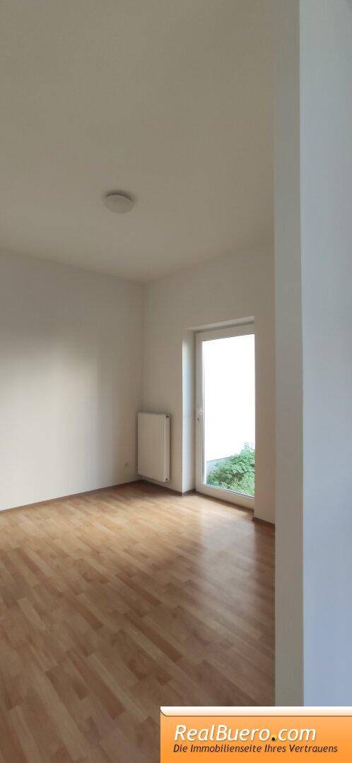 Helles Zimmer mit Holzboden und großem Fenster, das viel Tageslicht hereinlässt und den Raum erhellt.