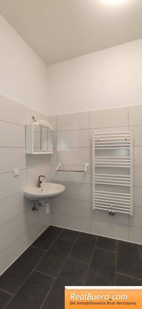 Modernes Badezimmer mit Waschbecken, Fliesenboden und beheiztem Handtuchhalter in schlichtem Design.