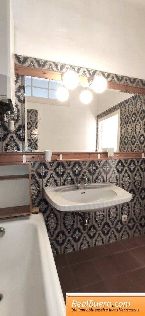 Badezimmer mit Waschbecken, großem Spiegel und gemusterten Fliesen, die einen traditionellen Stil zeigen.