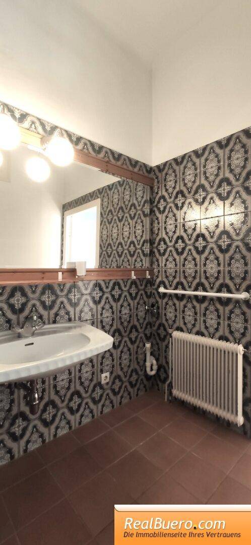 Badezimmer mit Heizkörper, Waschbecken und auffälligen gemusterten Fliesen an den Wänden.