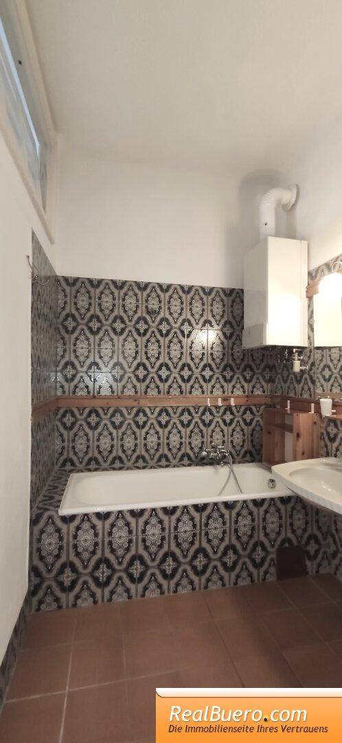 Badezimmer mit Badewanne, gemusterten Wandfliesen und braunem Fliesenboden.