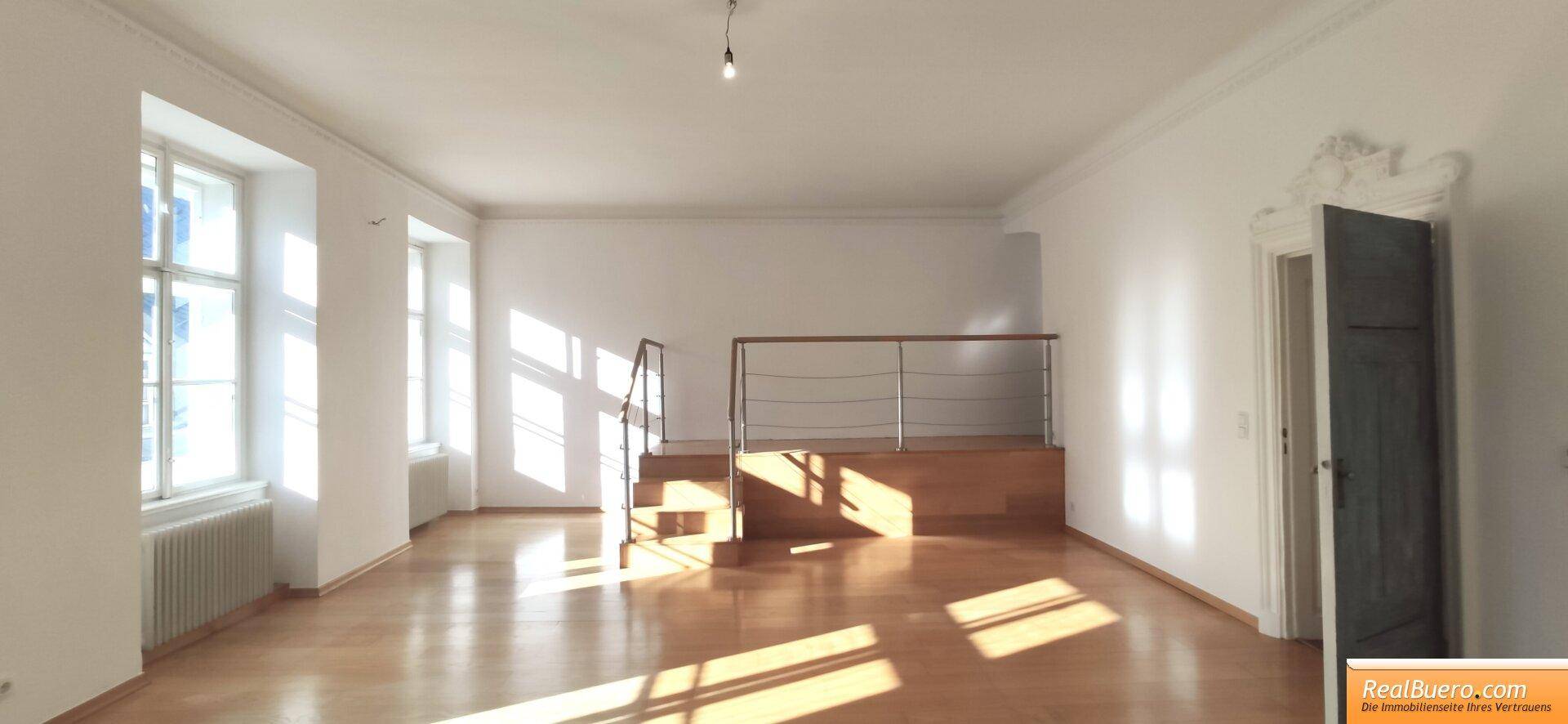 Geräumiges Wohnzimmer mit Holzboden, viel Tageslicht und einer dekorativen Türverzierung.