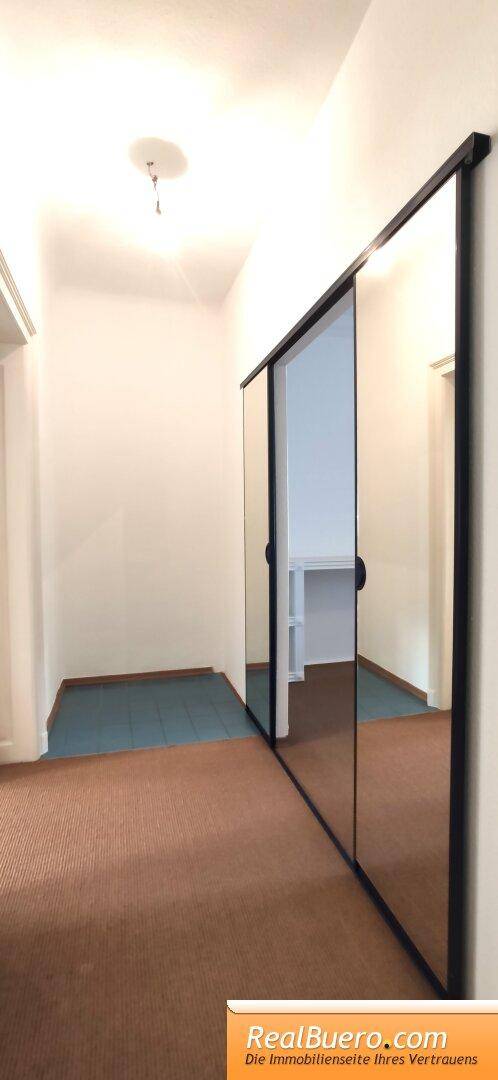 Langer Flur mit Teppichboden und einer reflektierenden Spiegelschiebetür, die Helligkeit spendet.