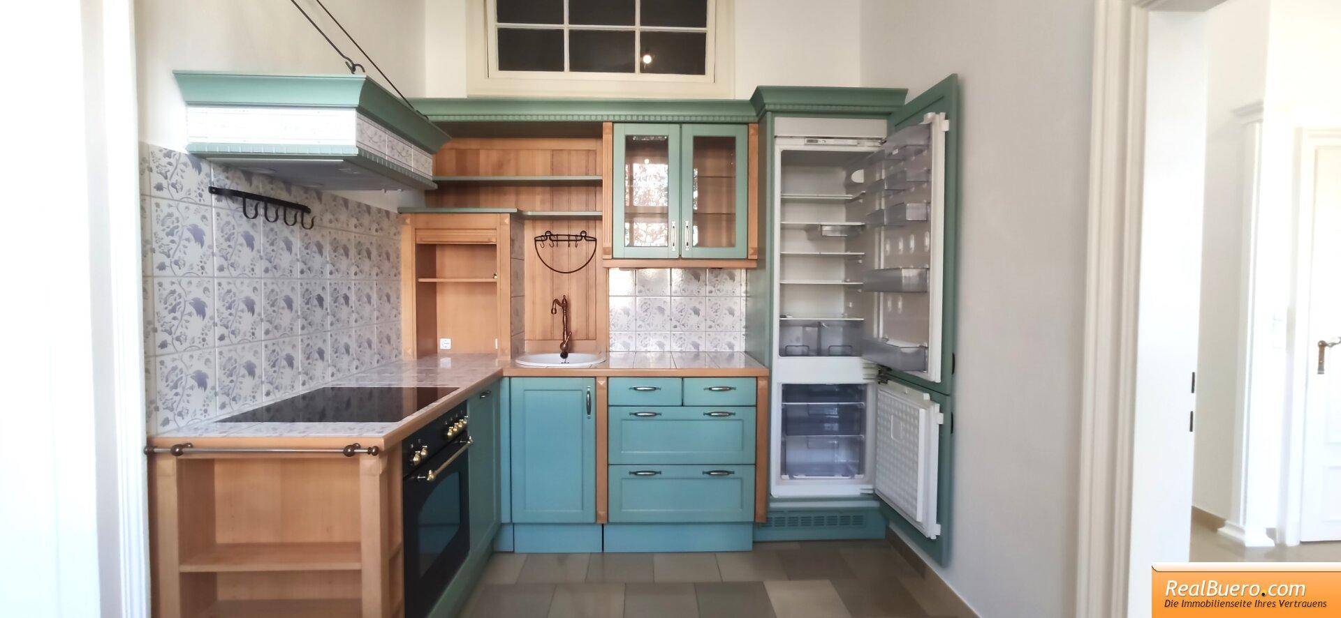 Voll ausgestattete Küche mit türkisfarbenen Schränken, integriertem Kühlschrank und gemusterten Wandfliesen.
