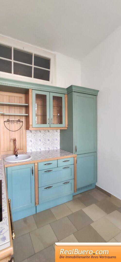 Küchenzeile mit Spülbecken, türkisfarbenen Schränken und einem hohen Schrank neben dem Fenster.