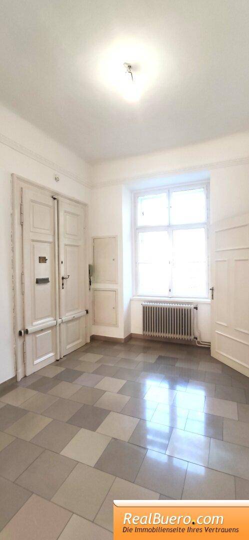 Geräumiger Flur mit Schachbrettmuster-Fliesenboden, hohen Türen und einem großen Fenster.