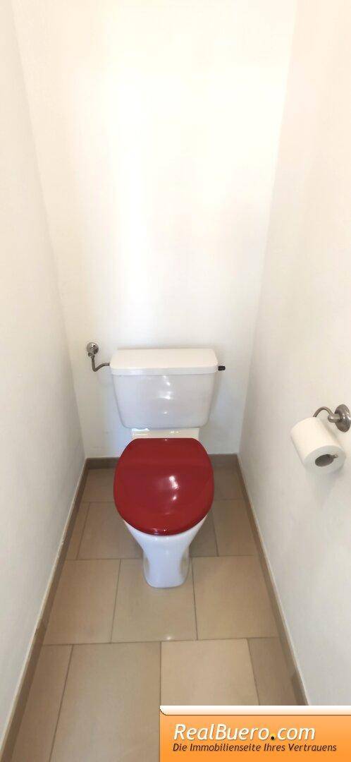 Separate Toilette mit rotem Toilettensitz und Fliesenboden in neutralen Farben.