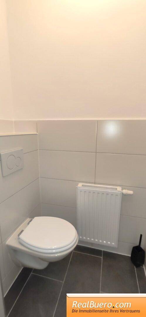 Schlichtes Gäste-WC mit Wand-WC, Heizkörper und dunklen Bodenfliesen für Besucher.