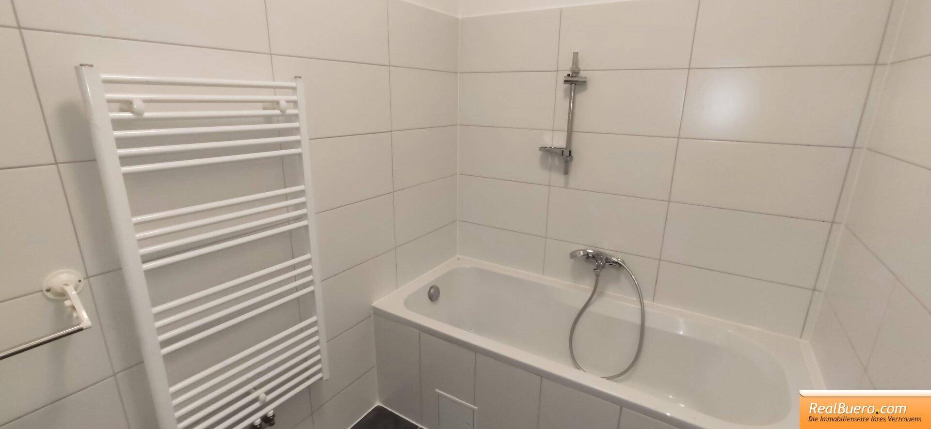 Badezimmer mit Badewanne, Duscharmatur und beheiztem Handtuchhalter, komplett mit weißen Fliesen.
