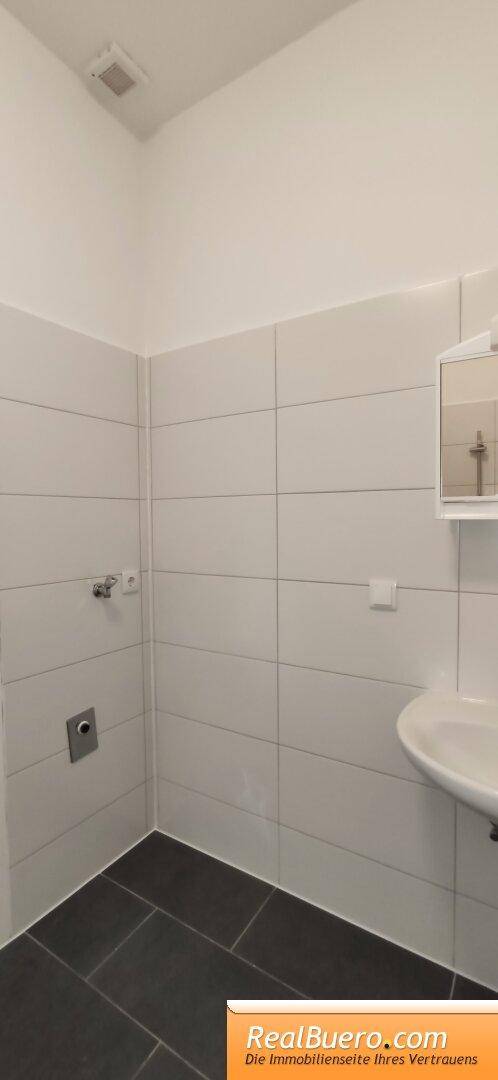 Teilansicht eines Badezimmers mit weißen Fliesen und dunklem Boden, bereit für die Einrichtung.