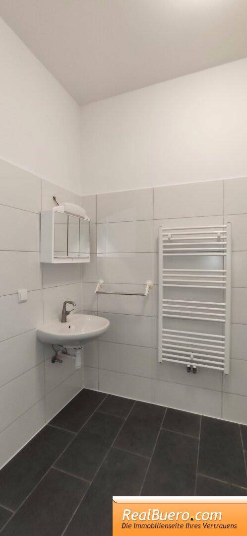 Modernes Badezimmer mit Waschbecken, Fliesenboden und beheiztem Handtuchhalter in heller Ausführung.