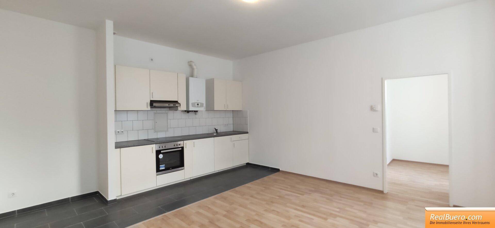 Geräumiger Wohn- und Essbereich mit offener Küche, Holzboden und hellen Wänden, ideal für Geselligkeit.