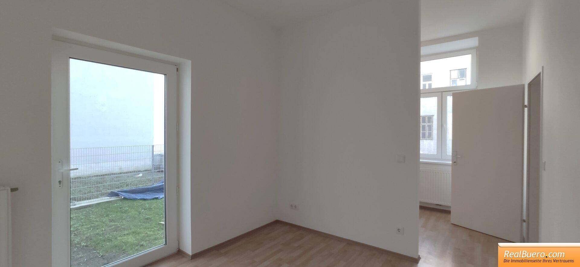 Helles Zimmer mit Zugang zu einem Außenbereich und Holzboden, ideal als Schlafzimmer oder Büro.