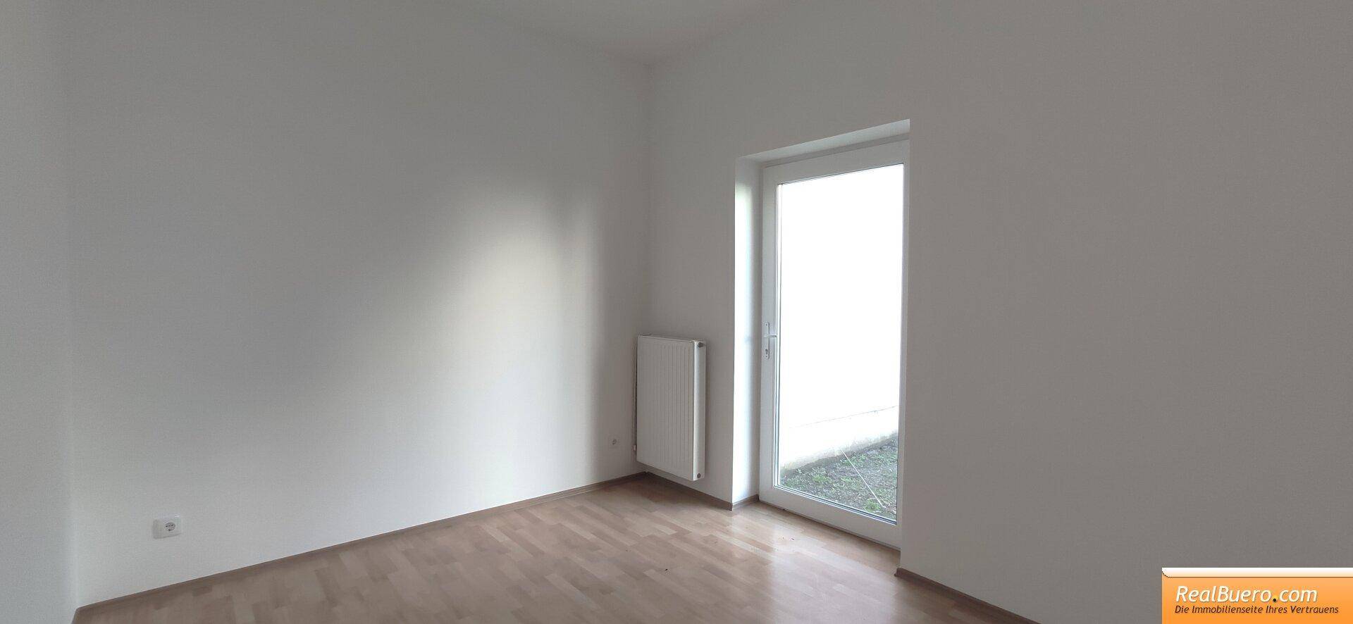 Helles Zimmer mit Holzboden und großem Fenster, das den Raum freundlich und einladend wirken lässt.