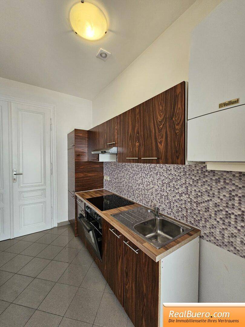 Praktische Küche mit Holzoptik-Schränken, Fliesenboden und einem Wandheizkessel der Marke Vaillant.