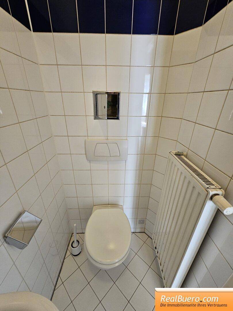 Kleines WC mit weißen Fliesen, wandhängender Toilette und Heizkörper, akzentuiert durch blaue Bordüren.