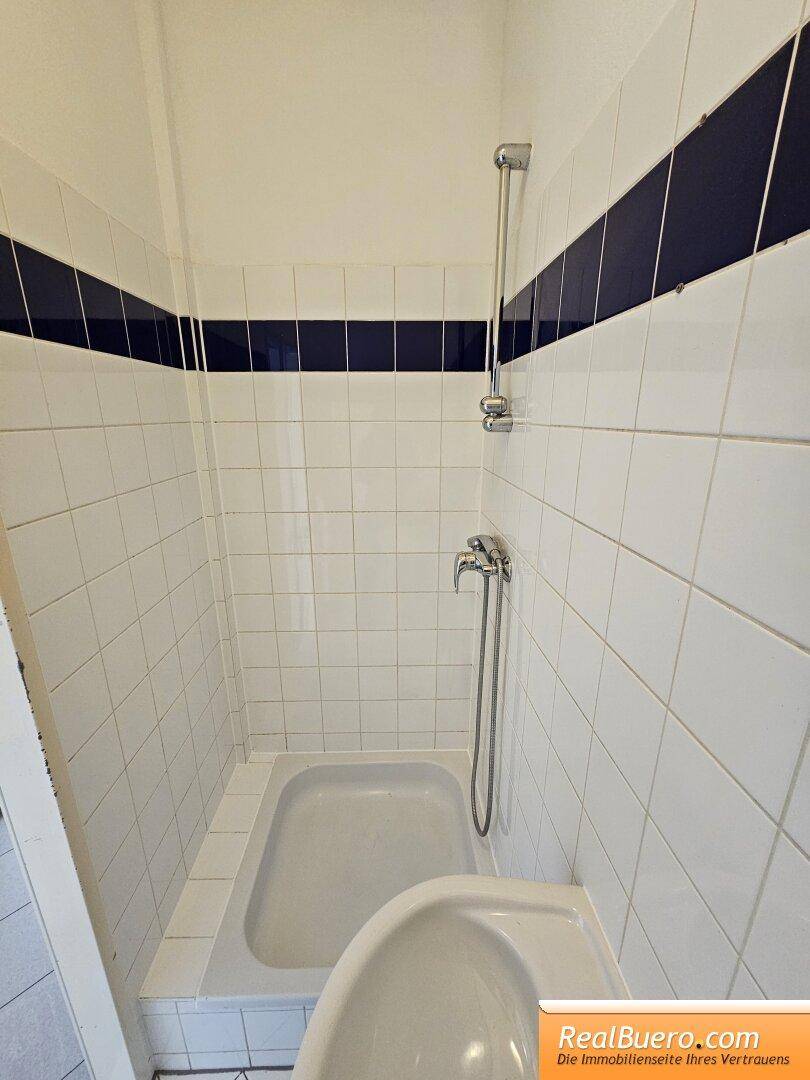 Kompakte Dusche mit weißen Wandfliesen und einem blauen Dekorstreifen, ausgestattet mit einer Handbrause.