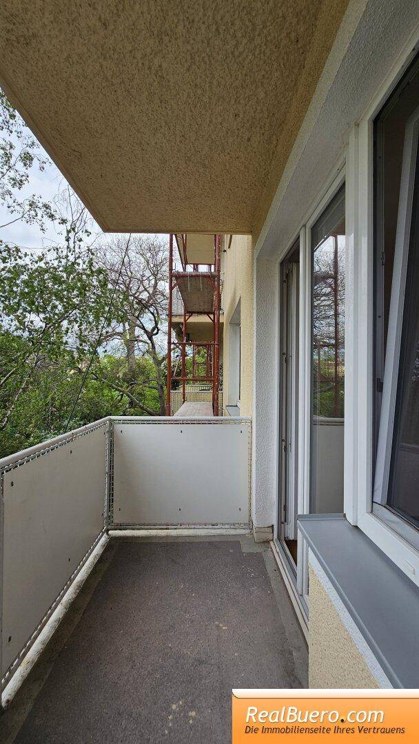 Kleiner Balkon mit Blick ins Grüne und angrenzendem Baugerüst an der Fassade.