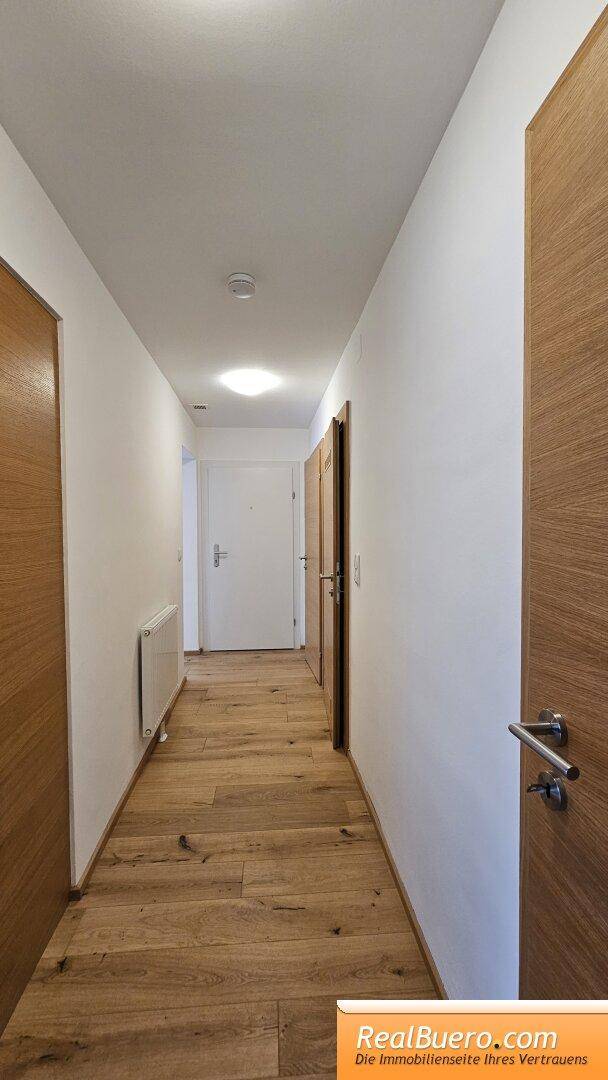 Langer Flur mit Holzboden, weißen Wänden und mehreren Holztüren zu den Zimmern.