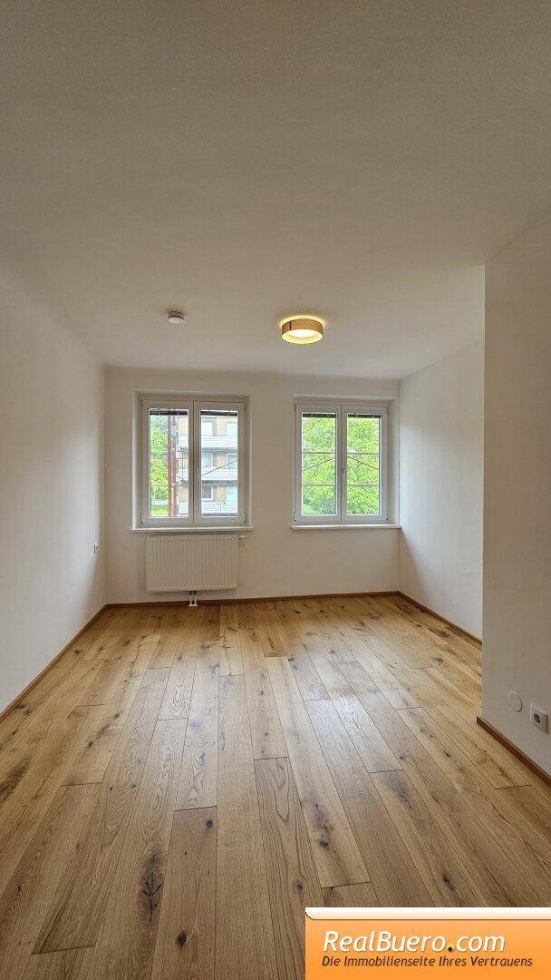 Helles Schlafzimmer mit zwei Fenstern, Holzboden und weißen Wänden, bereit zur Einrichtung.