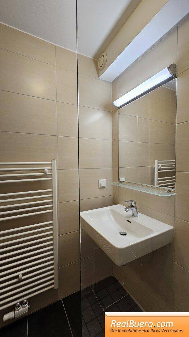 Modernes Badezimmer mit beigen Fliesen, Waschbecken und beheiztem Handtuchhalter.
