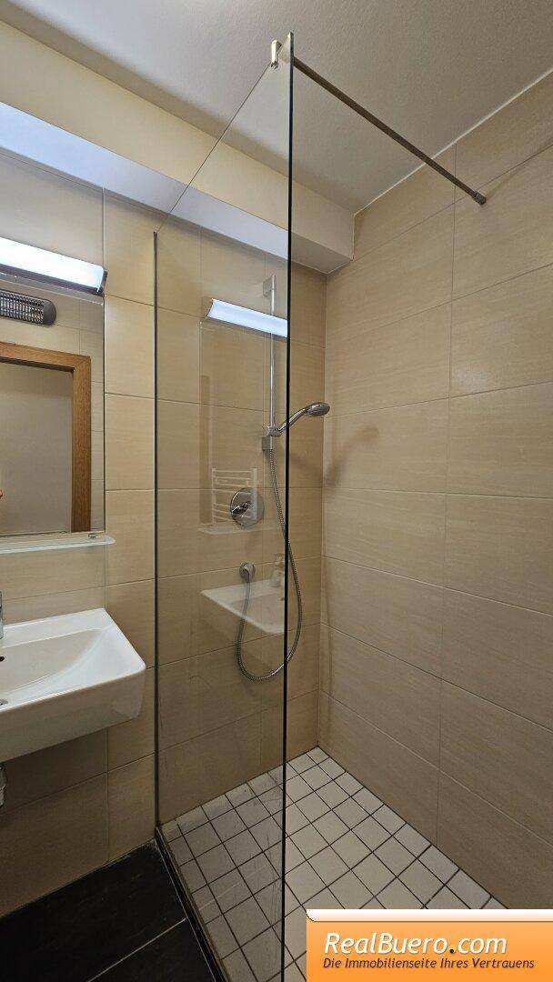Duschbereich im Badezimmer mit Glasabtrennung, beigen Wandfliesen und Duschkopf.