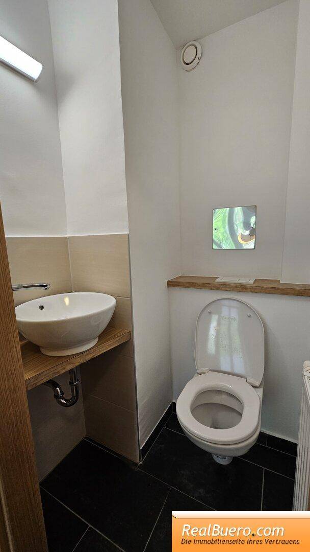 Separate Toilette mit Waschbecken, Wand-WC und Deckenlüftung für Gäste.
