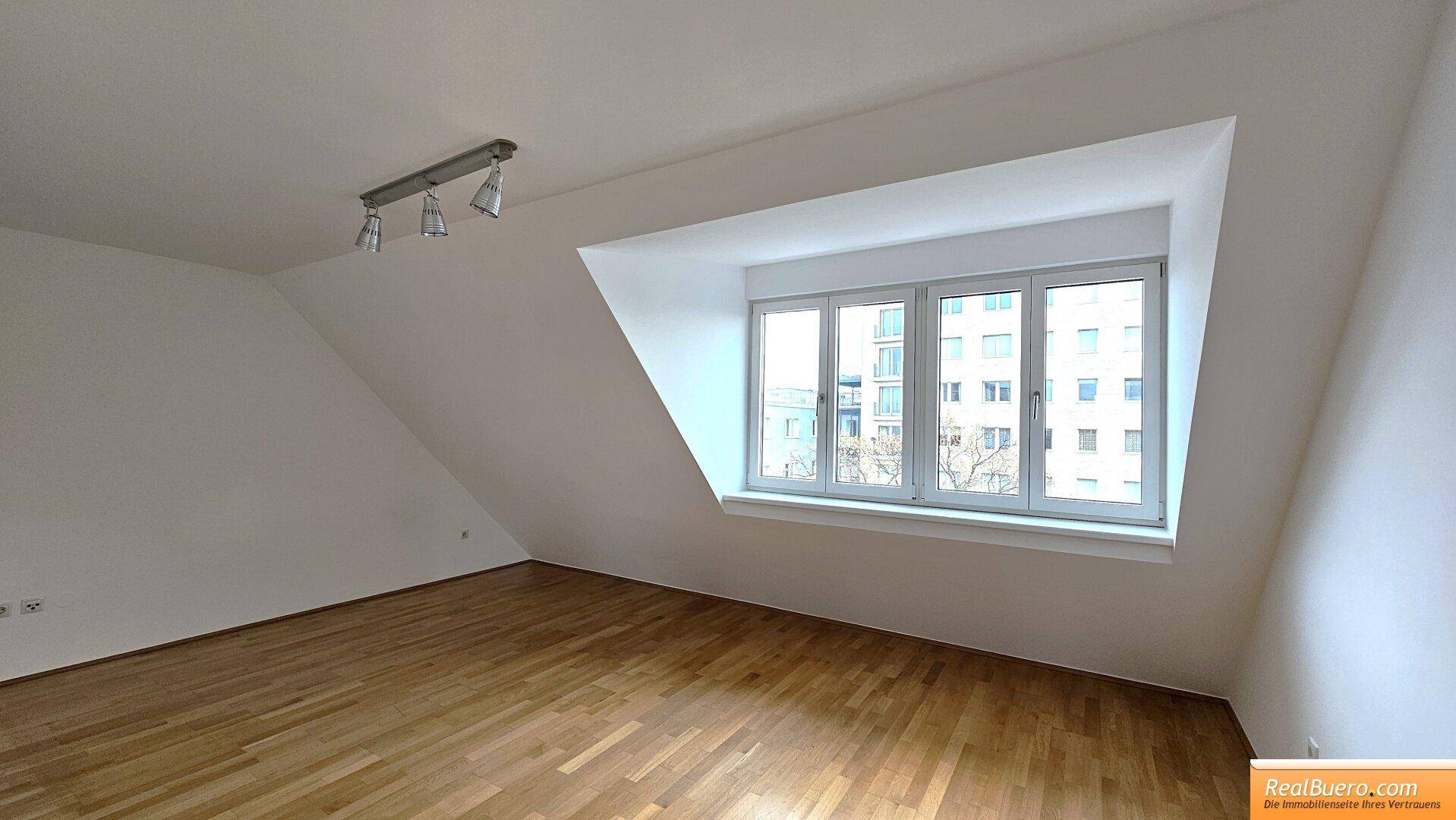 Helles Zimmer mit Parkettboden, weißen Wänden und einem großen Dachfenster.