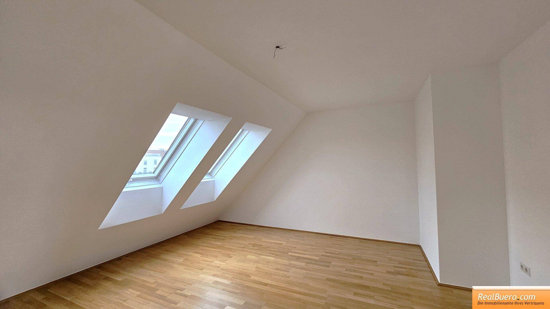 Helles Zimmer mit Parkettboden, weißen Wänden und zwei schrägen Dachfenstern.