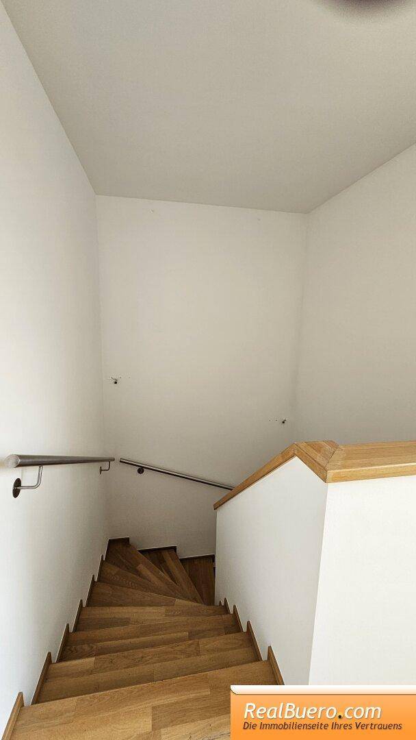 Holztreppe mit Geländer führt zu den oberen Etagen, umgeben von hellen Wänden.