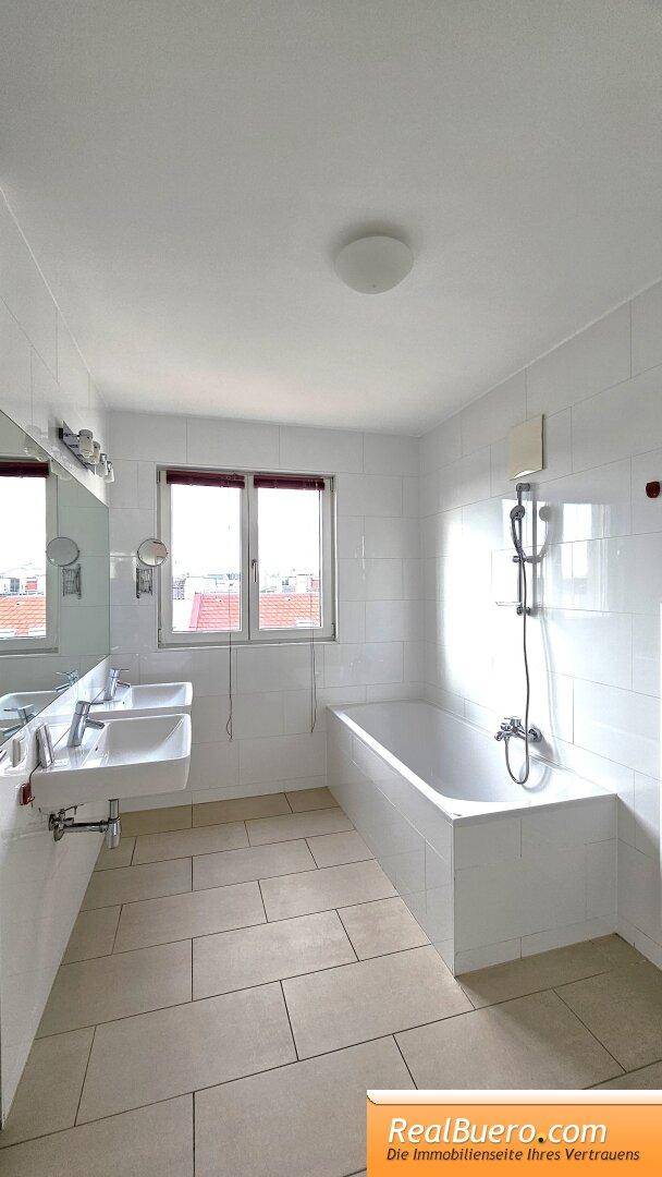 Geräumiges Badezimmer mit Badewanne, Doppelwaschbecken, Fenster und Fliesenboden.