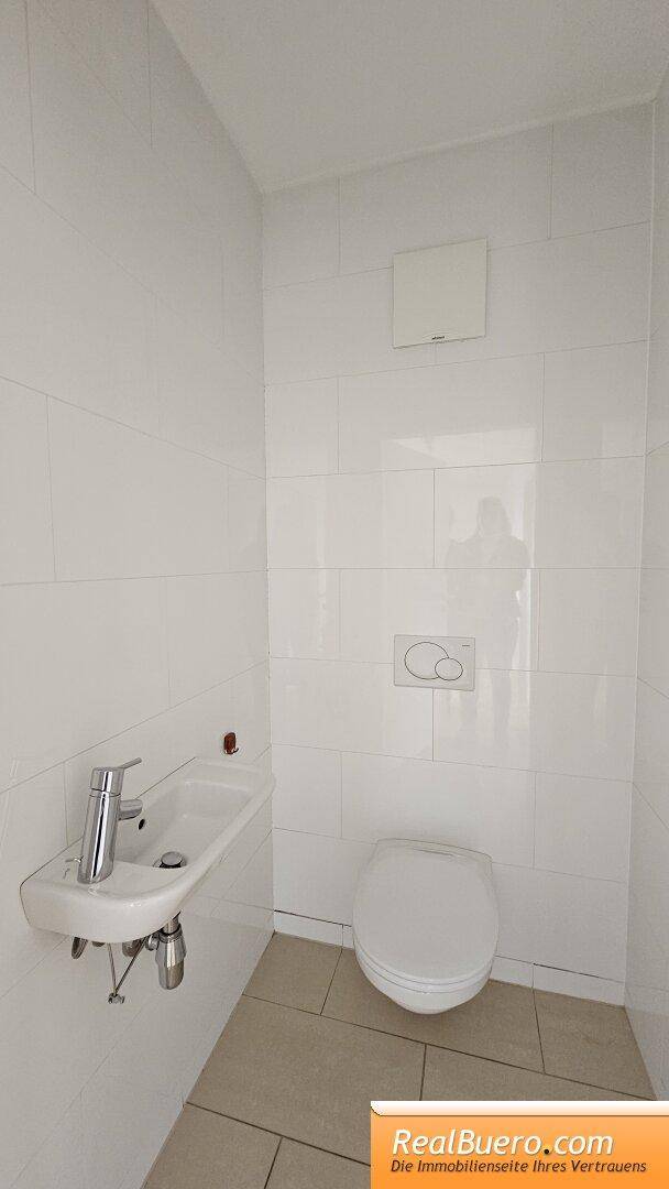 Schlichte Gästetoilette mit wandhängendem WC, kleinem Waschbecken und weißen Fliesen.