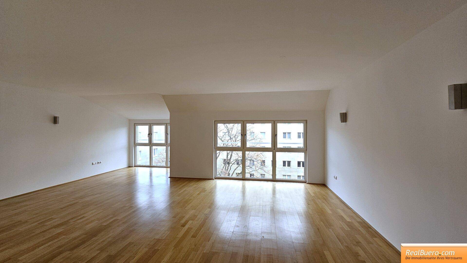 Helles, geräumiges Wohnzimmer mit großen Fenstern und glänzendem Parkettboden.