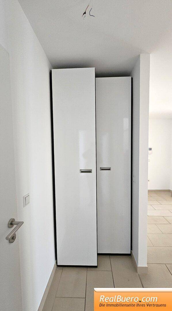 Heller Flur mit weißen, glänzenden Einbauschränken und Fliesenboden.