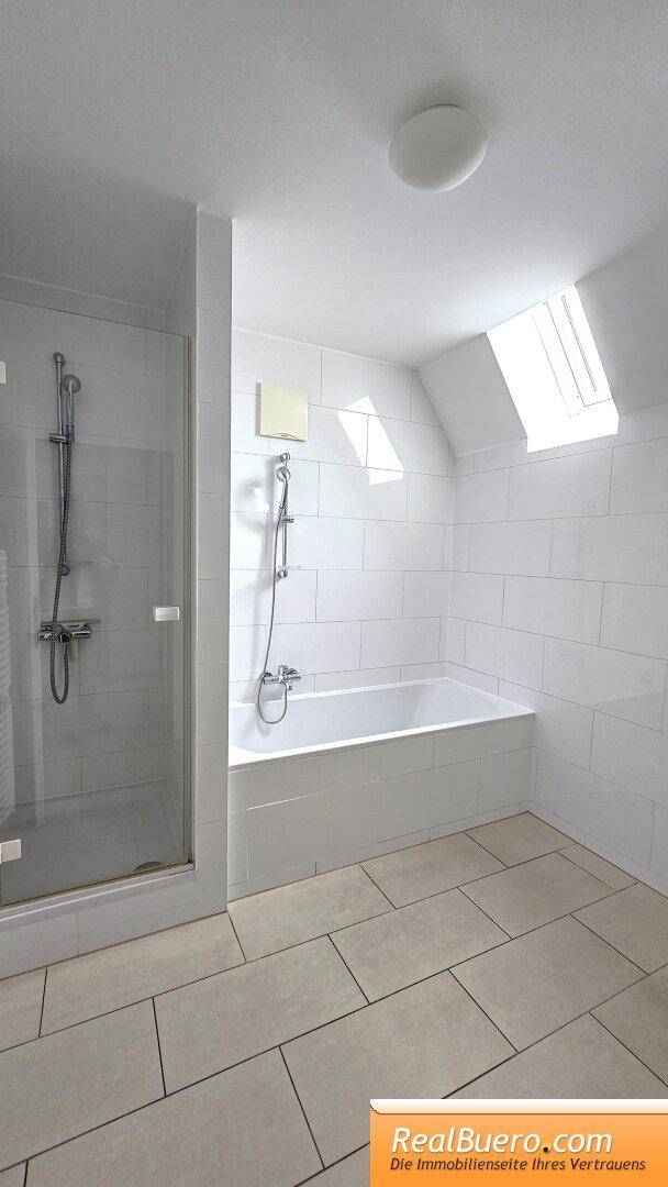 Modernes Badezimmer mit Badewanne, Duschkabine, Fliesenboden und Dachfenster.