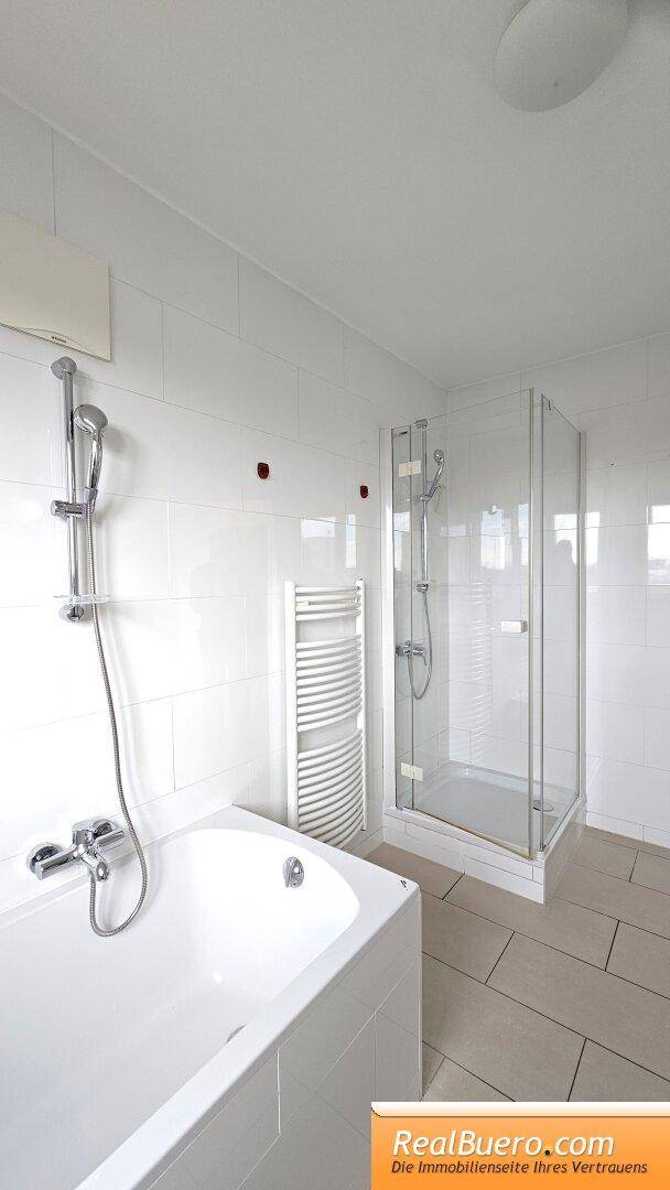 Helles Badezimmer mit Badewanne, Duschkabine, beheiztem Handtuchhalter und Fliesenboden.