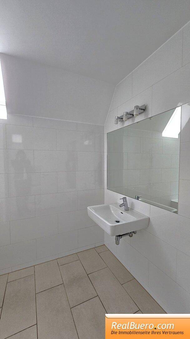 Helles Badezimmer mit modernem Waschbecken, großem Spiegel und weißen Fliesen.