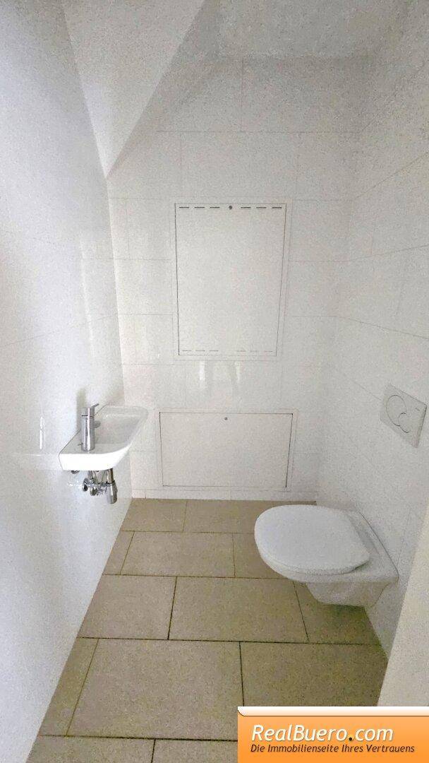 Separate Gästetoilette mit wandhängendem WC, kleinem Waschbecken und weißen Fliesen.
